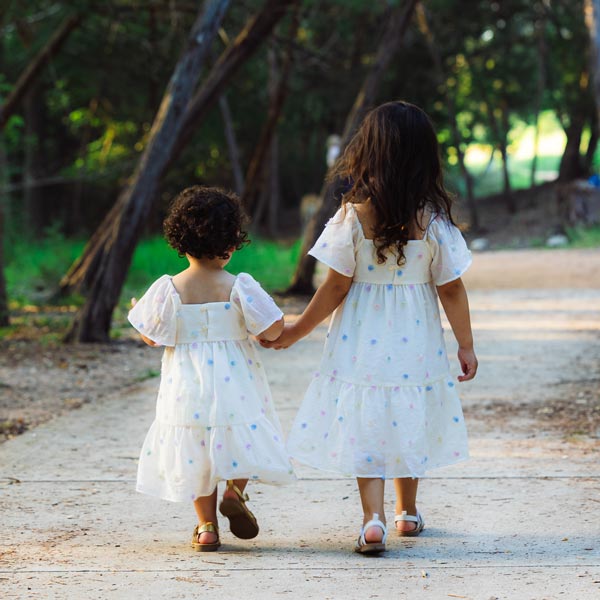 Two young girls in matching white dresses walk hand in hand in Dripping Springs, TX